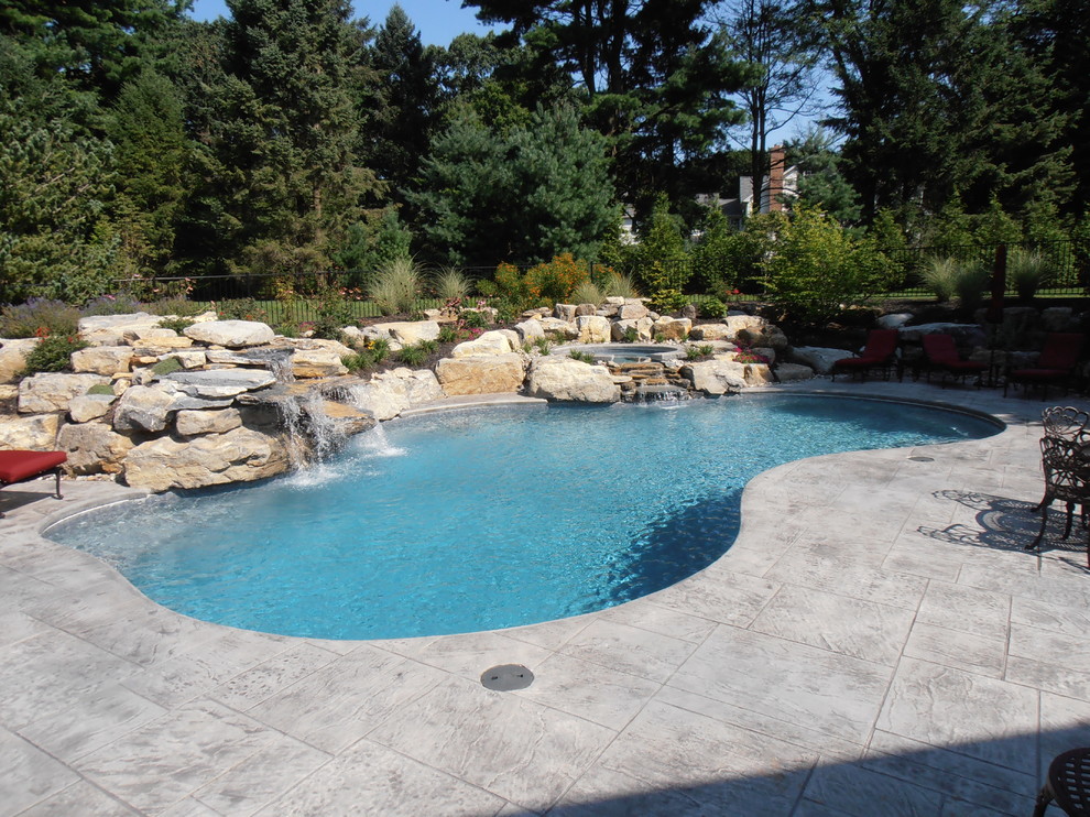 Traditional backyard custom-shaped natural pool in Philadelphia with stamped concrete and a hot tub.