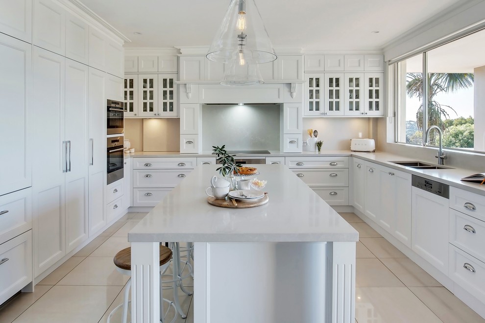 Large traditional u-shaped eat-in kitchen in Sydney with a double-bowl sink, recessed-panel cabinets, white cabinets, marble benchtops, white splashback, stainless steel appliances, porcelain floors, with island, white floor and white benchtop.