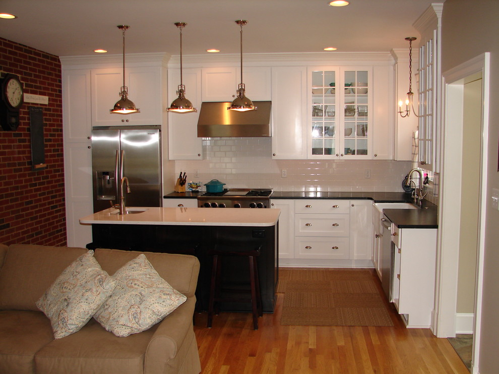 Example of a mid-sized transitional l-shaped light wood floor eat-in kitchen design in DC Metro with a farmhouse sink, white cabinets, granite countertops, white backsplash, ceramic backsplash, stainless steel appliances and an island