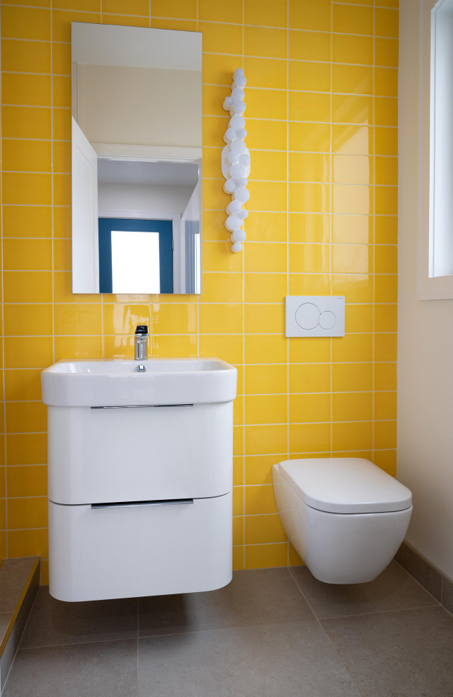 Modernes Badezimmer mit weißen Schränken, Wandtoilette, gelben Fliesen, Keramikfliesen, gelber Wandfarbe, Porzellan-Bodenfliesen, grauem Boden, Einzelwaschbecken, schwebendem Waschtisch, flächenbündigen Schrankfronten und Waschtischkonsole in Boston