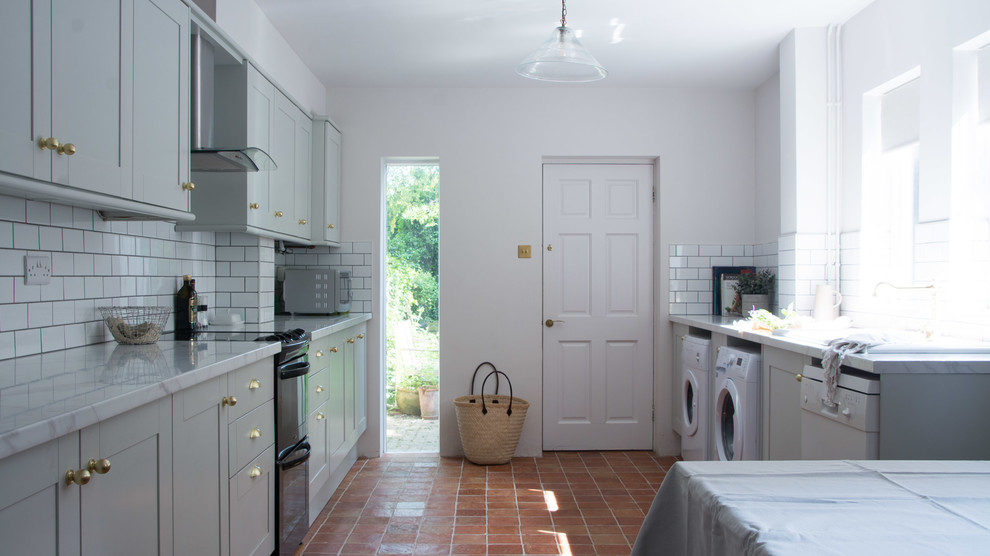 Mid-sized traditional galley eat-in kitchen in Cambridgeshire with a double-bowl sink, shaker cabinets, grey cabinets, laminate benchtops, white splashback, ceramic splashback, black appliances, terra-cotta floors, no island, orange floor and white benchtop.