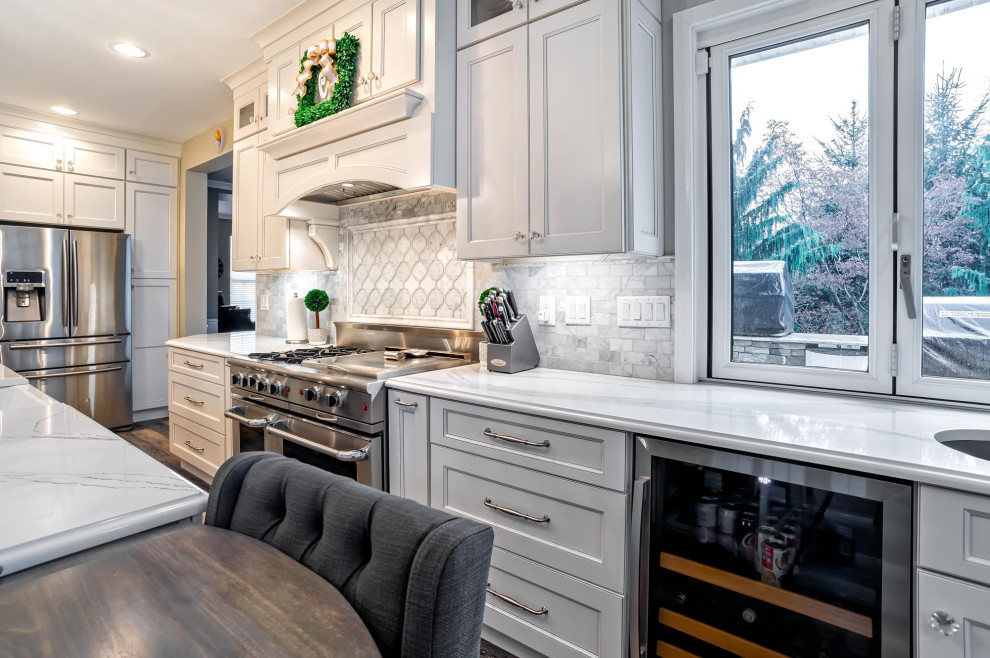 Large transitional single-wall medium tone wood floor and brown floor eat-in kitchen photo in Philadelphia with a farmhouse sink, shaker cabinets, white cabinets, quartz countertops, gray backsplash, porcelain backsplash, stainless steel appliances, an island and white countertops