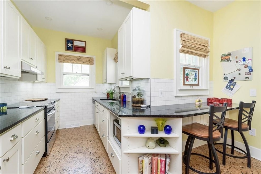 Mid-sized arts and crafts galley separate kitchen in Indianapolis with recessed-panel cabinets, white cabinets, quartz benchtops, black splashback, subway tile splashback, stainless steel appliances, cork floors, no island, brown floor and black benchtop.