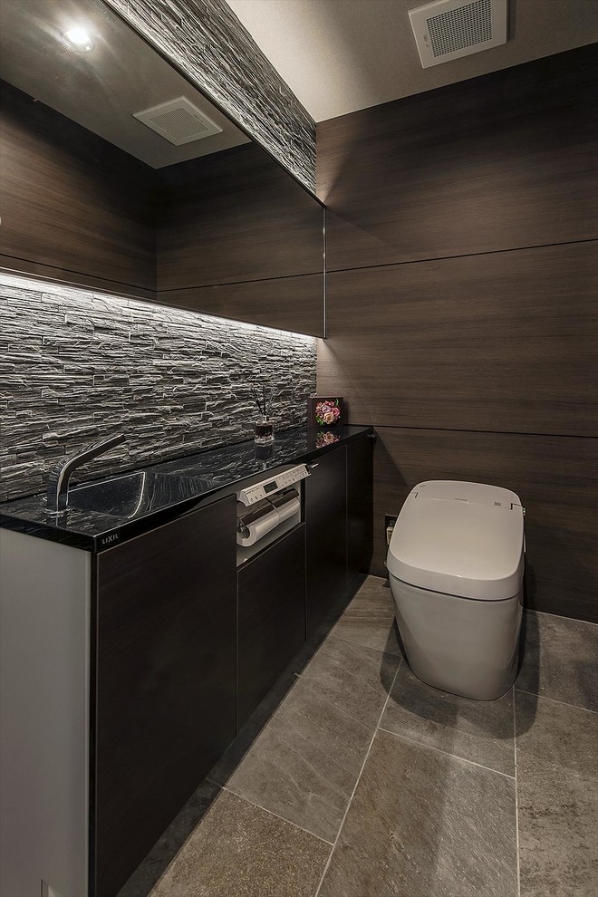 Photo of a modern powder room with flat-panel cabinets, brown cabinets, a one-piece toilet, grey floor, black benchtops and brown walls.