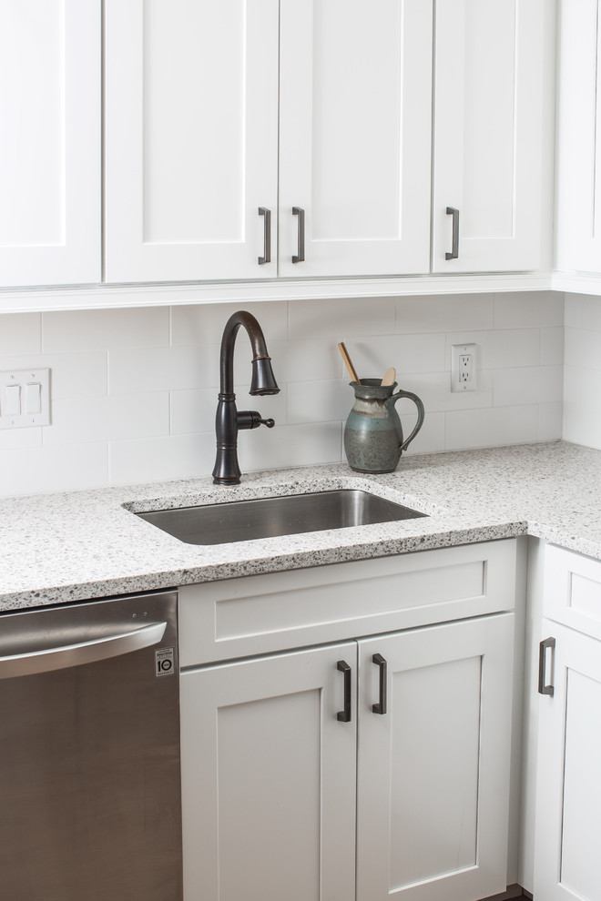This is an example of a small transitional u-shaped eat-in kitchen in Denver with an undermount sink, shaker cabinets, white cabinets, granite benchtops, white splashback, ceramic splashback, stainless steel appliances, vinyl floors, a peninsula, brown floor and beige benchtop.