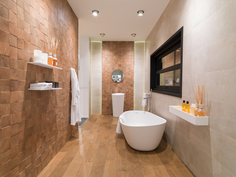 This is an example of a mid-sized contemporary 3/4 bathroom in Other with a freestanding tub, beige tile, brown tile, stone slab, beige walls, medium hardwood floors and a pedestal sink.