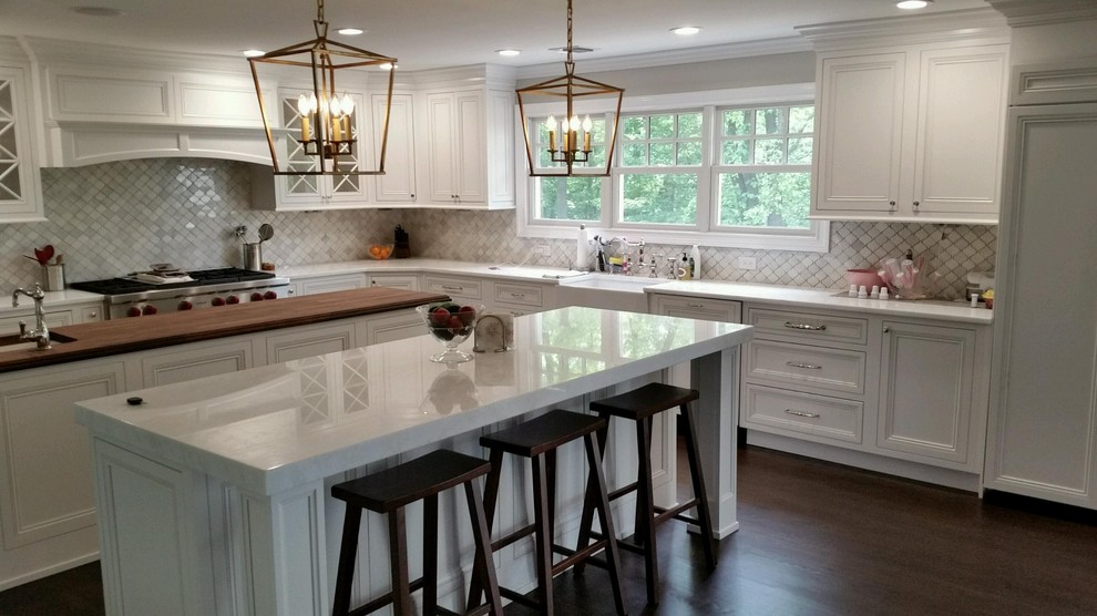 Huge transitional l-shaped dark wood floor kitchen pantry photo in New York with a farmhouse sink, shaker cabinets, white cabinets, marble countertops, white backsplash, porcelain backsplash, stainless steel appliances and two islands
