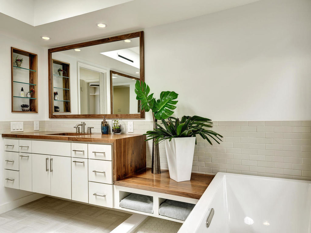 Photo of a mid-sized contemporary master bathroom in Austin with flat-panel cabinets, white cabinets, a drop-in tub, beige tile, ceramic tile, white walls, ceramic floors, an undermount sink and wood benchtops.