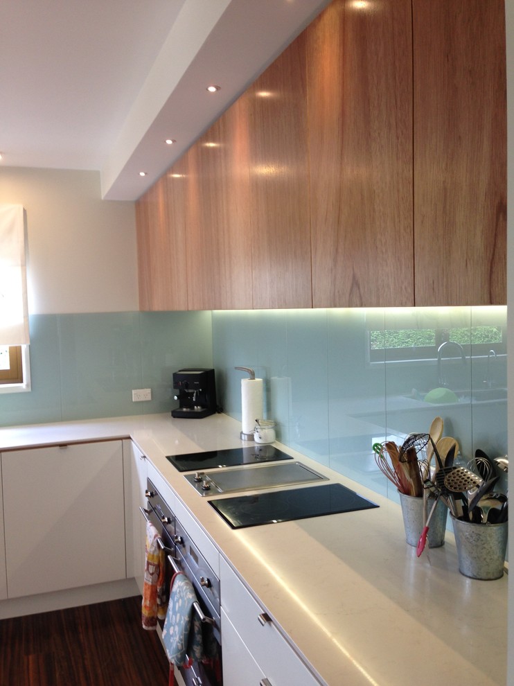 Photo of a large scandinavian u-shaped separate kitchen in Auckland with an undermount sink, flat-panel cabinets, quartz benchtops, glass sheet splashback, stainless steel appliances, laminate floors, with island and brown floor.