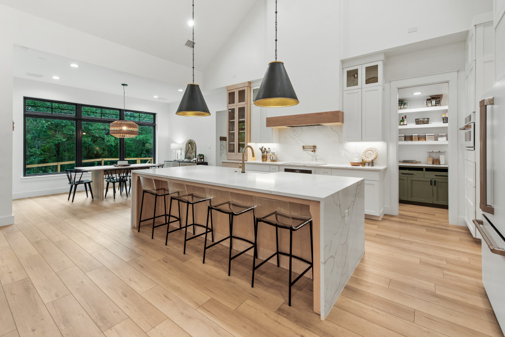 Photo of a mid-sized scandinavian l-shaped open plan kitchen in Dallas with a farmhouse sink, shaker cabinets, white cabinets, quartz benchtops, white splashback, engineered quartz splashback, white appliances, vinyl floors, with island, white benchtop and exposed beam.