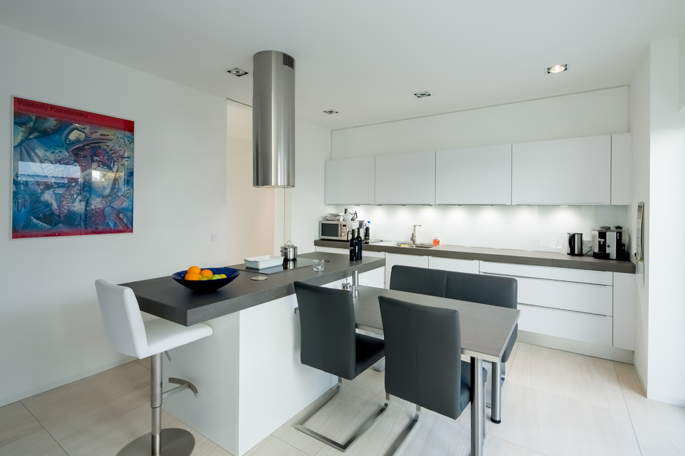 Inspiration for a mid-sized contemporary galley open plan kitchen in Dusseldorf with an undermount sink, flat-panel cabinets, white cabinets, solid surface benchtops, white splashback, glass sheet splashback, black appliances, ceramic floors and with island.