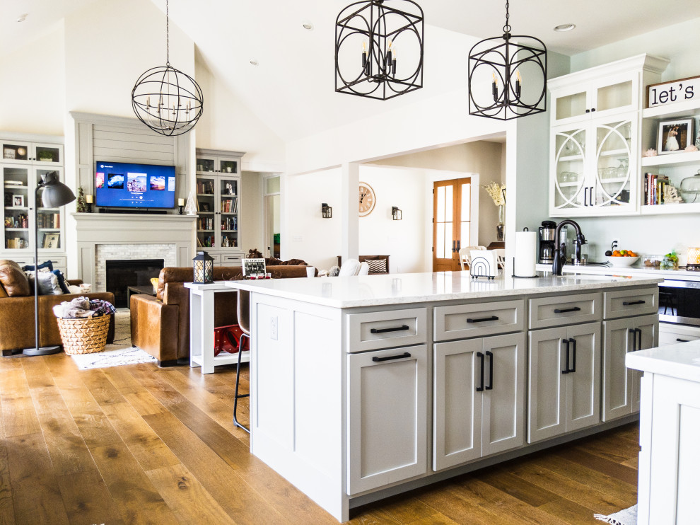 Design ideas for a large country u-shaped open plan kitchen in Indianapolis with a farmhouse sink, shaker cabinets, white cabinets, quartz benchtops, green splashback, stainless steel appliances, medium hardwood floors, with island and white benchtop.