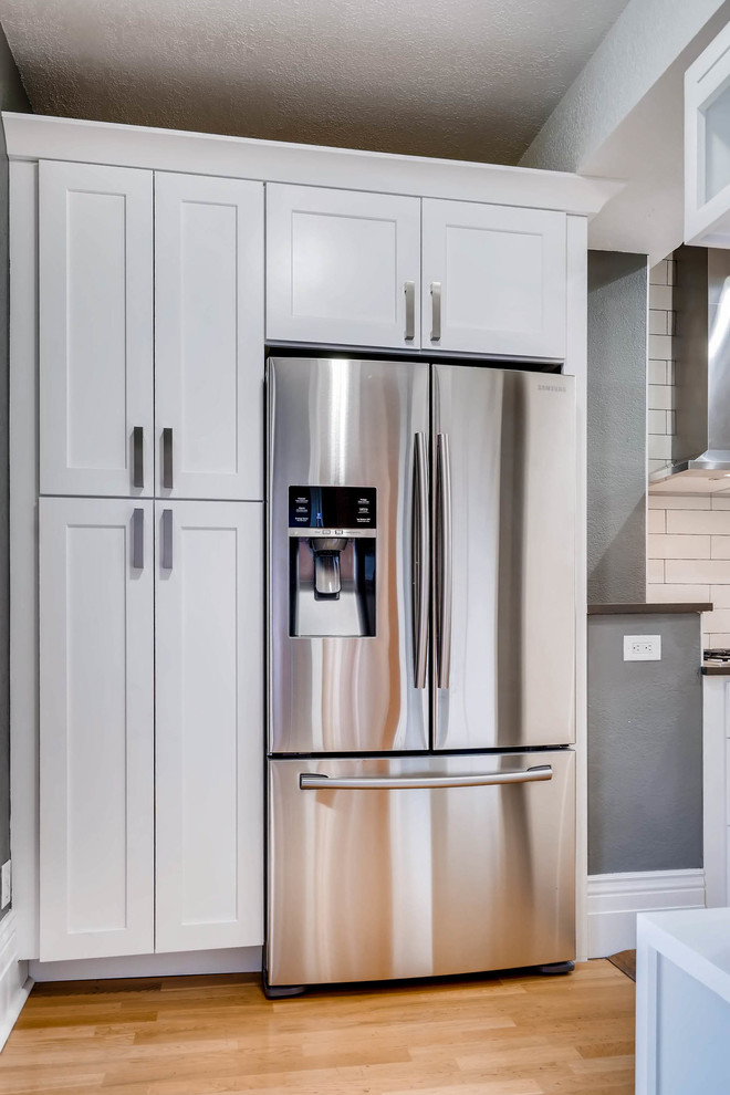 Eat-in kitchen - large rustic light wood floor and brown floor eat-in kitchen idea in Denver with a farmhouse sink, shaker cabinets, white cabinets, quartz countertops, white backsplash, ceramic backsplash, stainless steel appliances, a peninsula and brown countertops