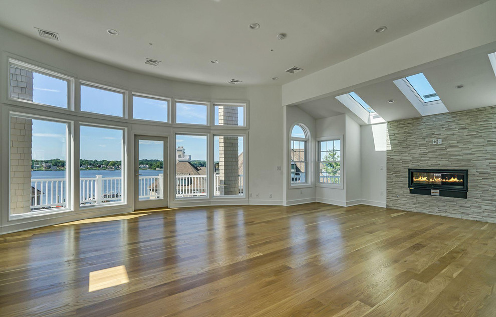 Expansive beach style open concept family room in Newark with a game room, white walls, light hardwood floors, a standard fireplace, a stone fireplace surround, a wall-mounted tv and brown floor.