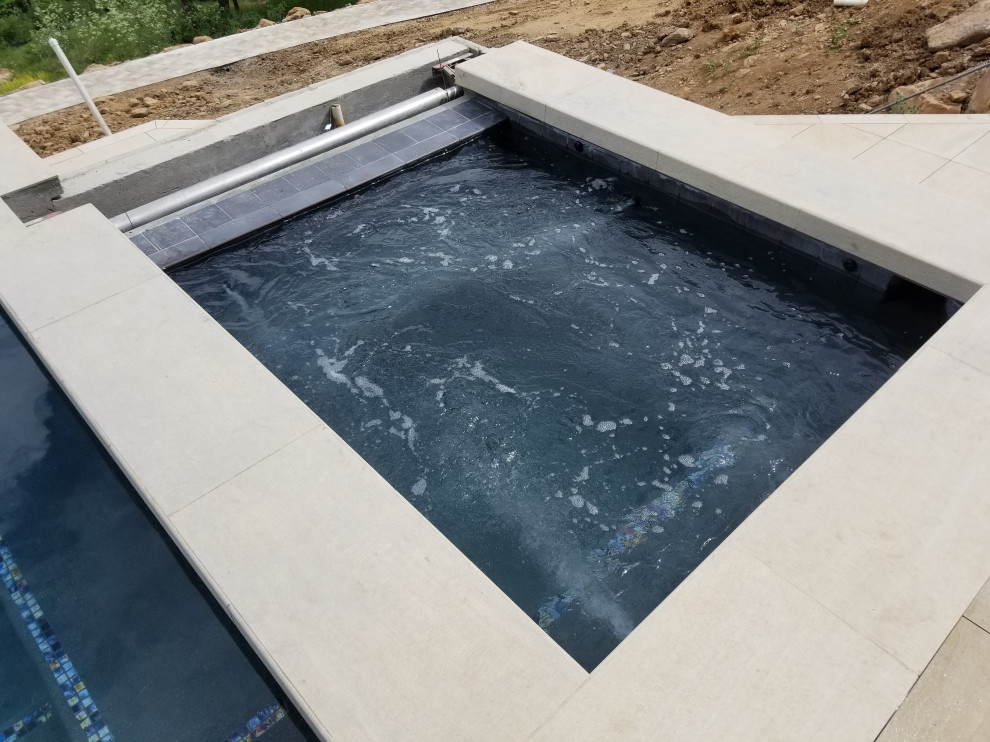 Example of a mid-sized backyard rectangular infinity hot tub design in Denver