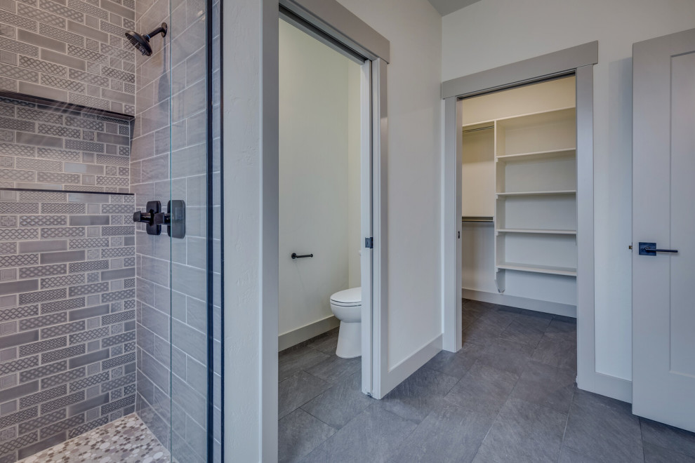 This is an example of a mid-sized country master bathroom in Other with recessed-panel cabinets, grey cabinets, a double shower, a two-piece toilet, gray tile, ceramic tile, white walls, ceramic floors, an undermount sink, engineered quartz benchtops, black floor, a hinged shower door, white benchtops, an enclosed toilet, a double vanity and a built-in vanity.