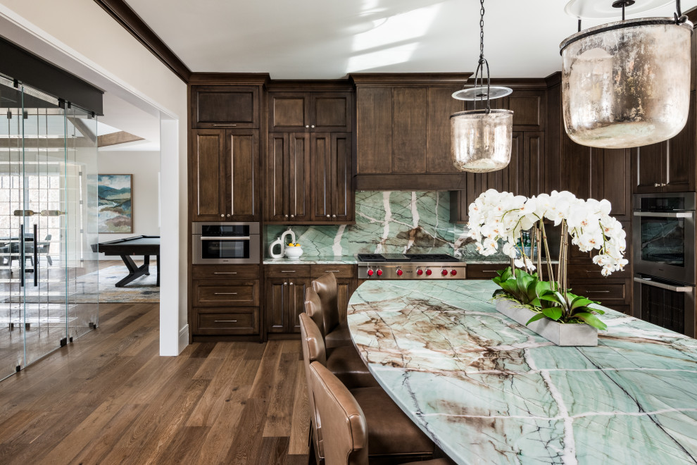 Large transitional u-shaped medium tone wood floor and brown floor enclosed kitchen photo with an undermount sink, flat-panel cabinets, dark wood cabinets, quartzite countertops, green backsplash, stone slab backsplash, paneled appliances, an island and green countertops