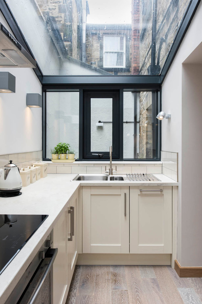 Design ideas for a transitional kitchen in Other with a drop-in sink, shaker cabinets, beige cabinets, beige splashback, subway tile splashback and light hardwood floors.