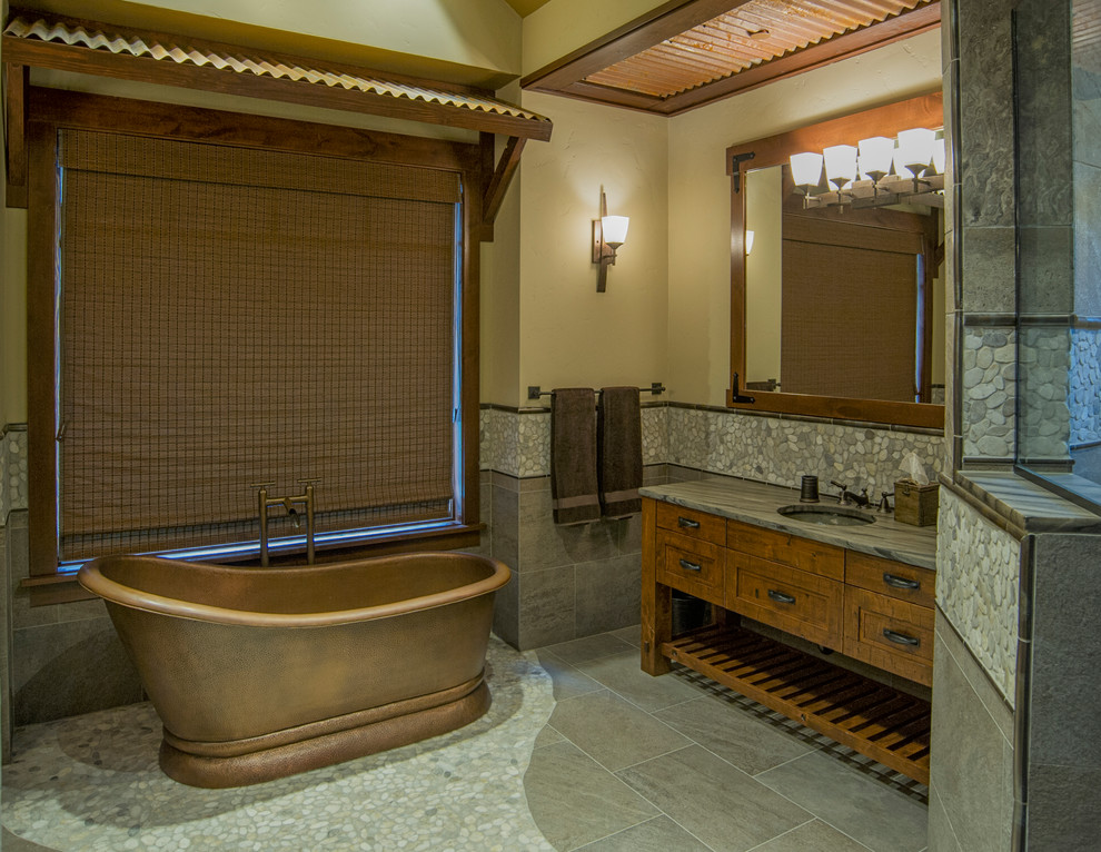 This is an example of a country master bathroom in Seattle with furniture-like cabinets, dark wood cabinets, a freestanding tub, an alcove shower, pebble tile, beige walls, porcelain floors, an undermount sink and a hinged shower door.