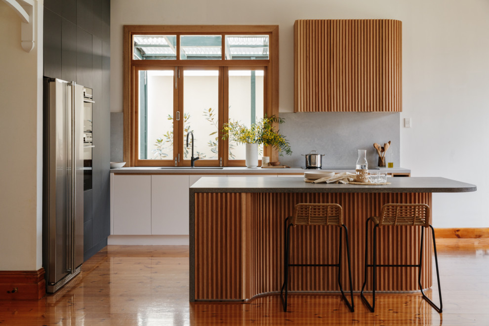 Mid-sized midcentury l-shaped eat-in kitchen in Adelaide with an undermount sink, flat-panel cabinets, black cabinets, solid surface benchtops, grey splashback, stone slab splashback, panelled appliances, light hardwood floors, with island, brown floor and grey benchtop.