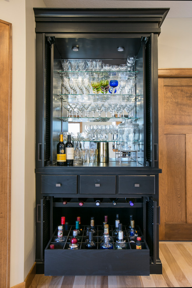 This is an example of a traditional home bar in Minneapolis with black cabinets, light hardwood floors and beige floor.