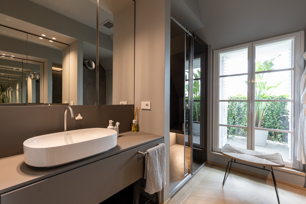 Modernes Badezimmer mit grauen Schränken, Wandtoilette, grauer Wandfarbe, hellem Holzboden, Aufsatzwaschbecken, beigem Boden, Schiebetür-Duschabtrennung, grauer Waschtischplatte, Doppelwaschbecken und schwebendem Waschtisch in Mailand
