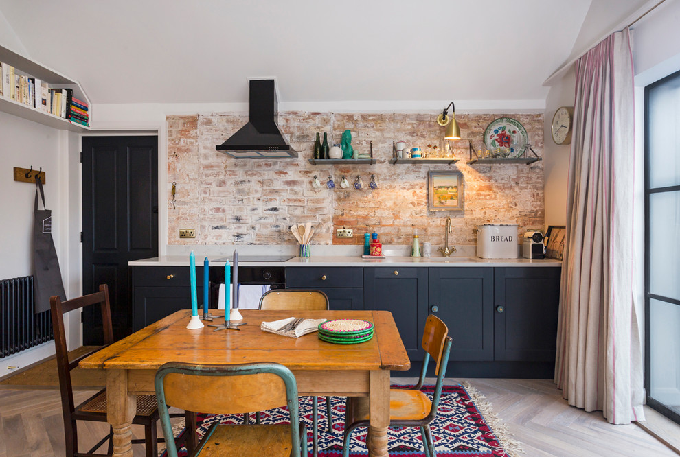 Eclectic single-wall eat-in kitchen in Kent with shaker cabinets, blue cabinets, red splashback, brick splashback, black appliances, light hardwood floors, no island and beige floor.