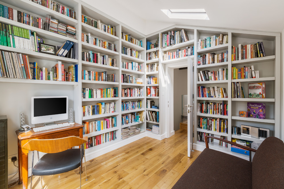 Photo of a contemporary home office in London with a library, medium hardwood floors, a freestanding desk and brown floor.