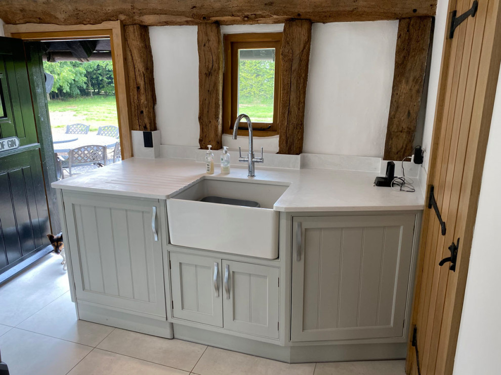 Inspiration for a large rustic l-shaped open plan kitchen in Essex with an integrated sink, shaker cabinets, grey cabinets, engineered stone countertops, white splashback, black appliances, ceramic flooring, an island, white floors, white worktops and feature lighting.