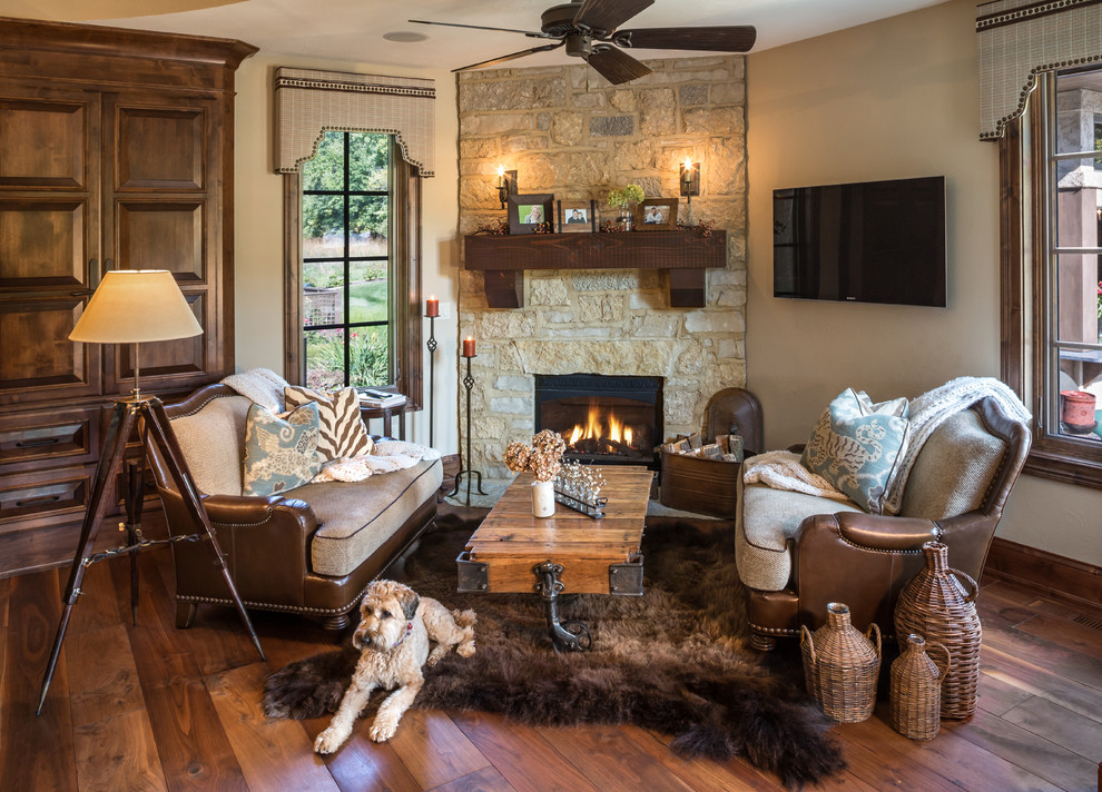 This is an example of a traditional family room in Milwaukee with beige walls, medium hardwood floors, a corner fireplace, a stone fireplace surround, a wall-mounted tv and brown floor.