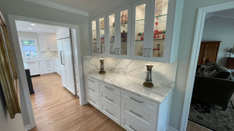Inspiration for a mid-sized transitional u-shaped light wood floor, brown floor and vaulted ceiling kitchen pantry remodel in Orange County with a double-bowl sink, shaker cabinets, white cabinets, granite countertops, white backsplash, marble backsplash, stainless steel appliances, an island and white countertops