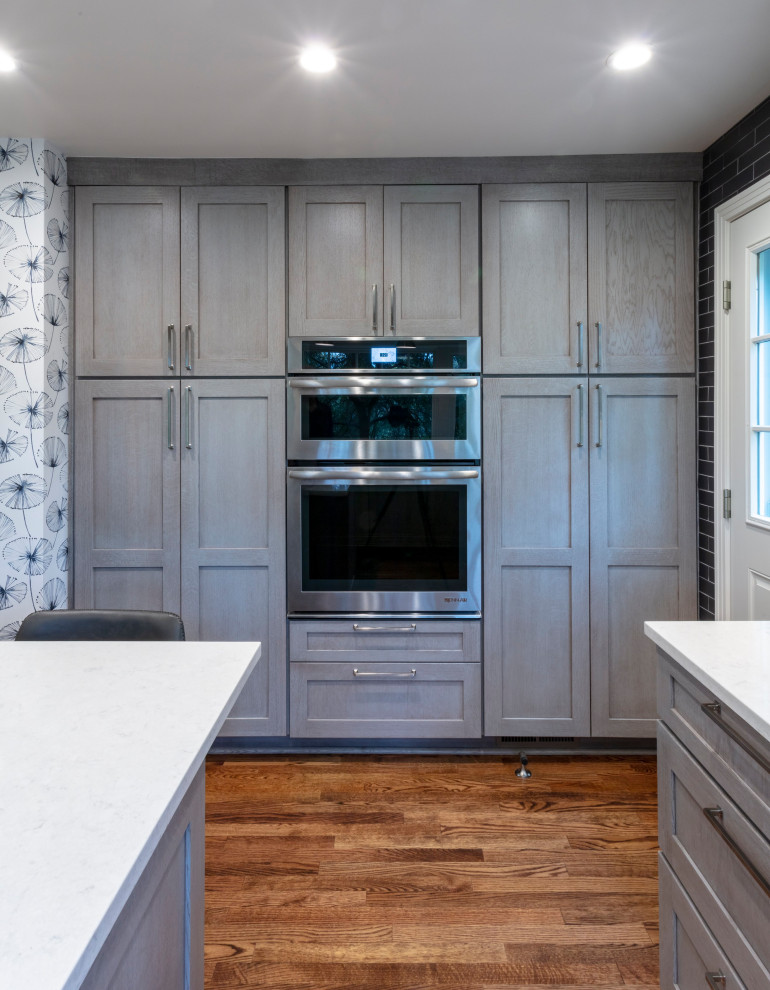 Inspiration for a contemporary u-shaped medium tone wood floor and brown floor eat-in kitchen remodel with an undermount sink, shaker cabinets, gray cabinets, quartz countertops, gray backsplash, ceramic backsplash, stainless steel appliances, an island and gray countertops