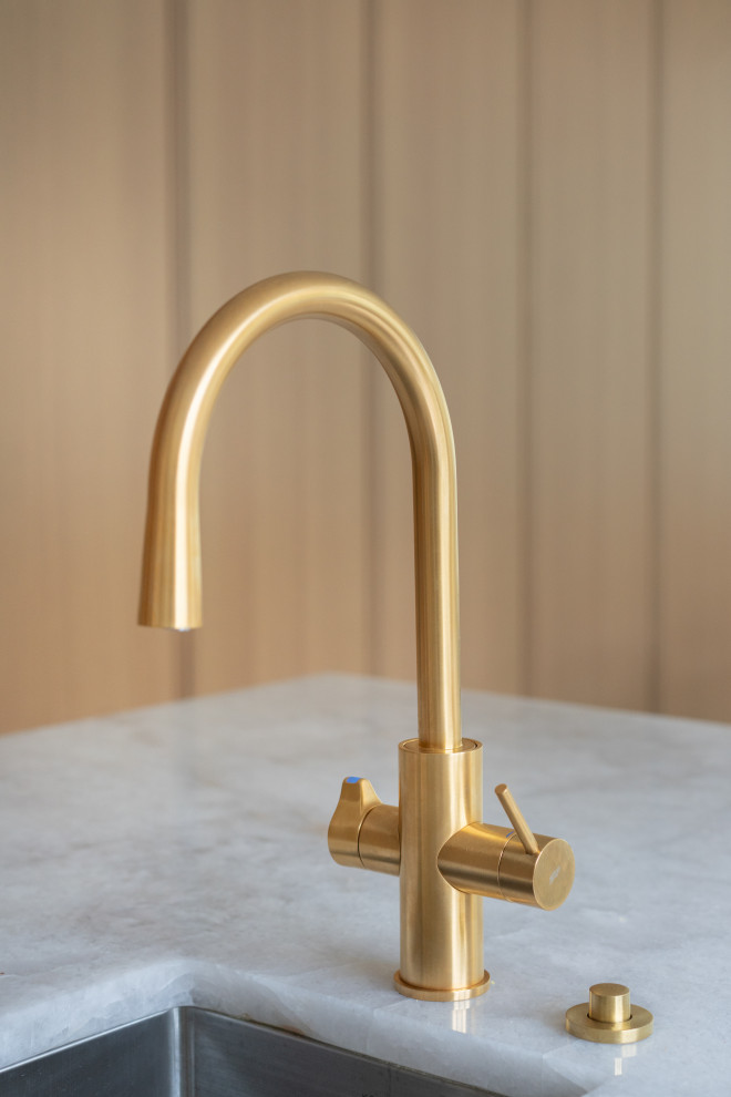 An elegant and modern kitchen faucet with a gold finish, placed near a large win