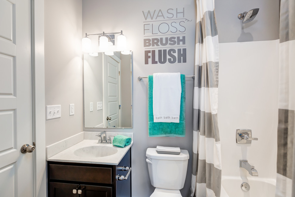 Mid-sized transitional kids' tub/shower combo photo with recessed-panel cabinets, dark wood cabinets, a one-piece toilet, gray walls, an integrated sink and marble countertops
