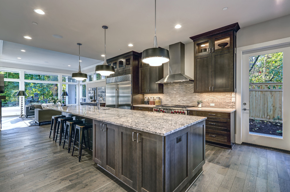 Inspiration for a large eclectic single-wall open plan kitchen in Baltimore with an undermount sink, recessed-panel cabinets, grey cabinets, granite benchtops, white splashback, stone tile splashback, stainless steel appliances, light hardwood floors, with island and grey floor.