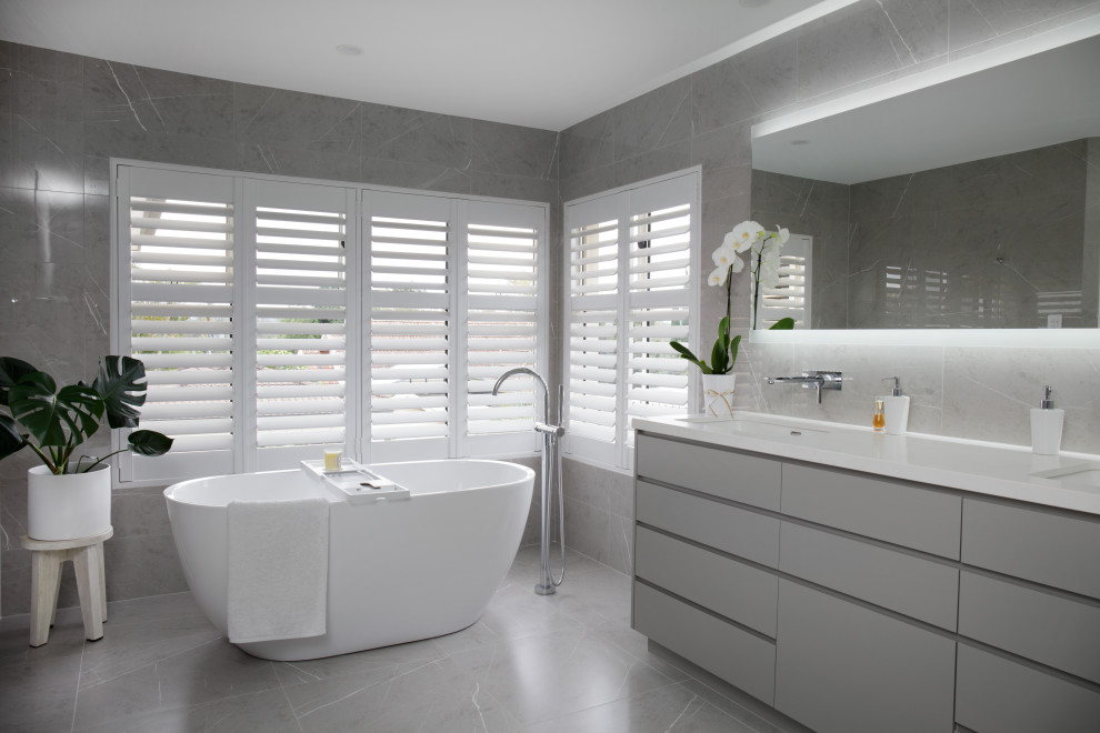 Inspiration for a large modern master bathroom in Brisbane with grey cabinets, a freestanding tub, gray tile, ceramic tile, grey walls, ceramic floors, engineered quartz benchtops, grey floor, white benchtops, a double vanity and a built-in vanity.