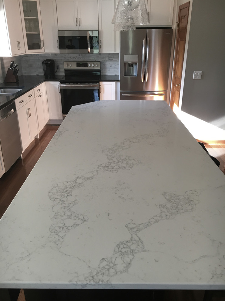 Example of a large transitional single-wall medium tone wood floor eat-in kitchen design with an undermount sink, shaker cabinets, white cabinets, granite countertops, multicolored backsplash, marble backsplash, stainless steel appliances, an island and black countertops