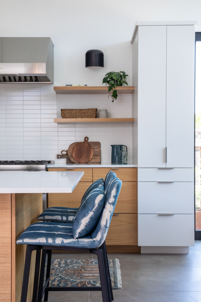 Example of a mid-sized mid-century modern galley porcelain tile, gray floor and shiplap ceiling eat-in kitchen design in San Francisco with a drop-in sink, flat-panel cabinets, light wood cabinets, quartz countertops, white backsplash, ceramic backsplash, stainless steel appliances, an island and white countertops