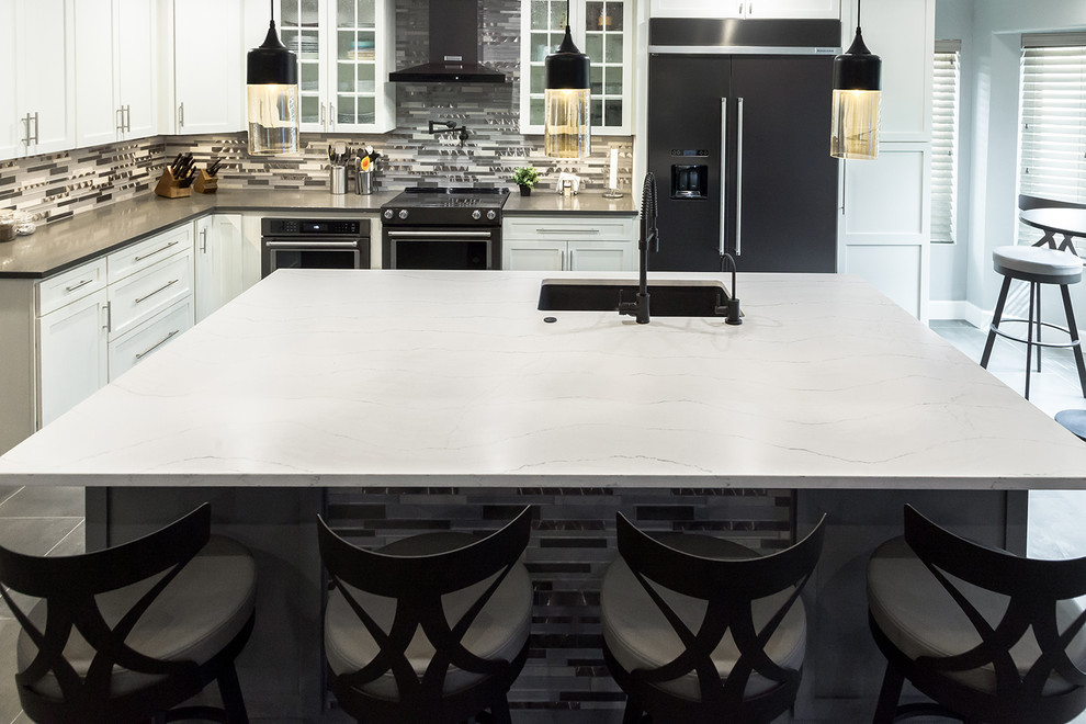 Example of a mid-sized transitional l-shaped porcelain tile and gray floor open concept kitchen design in Phoenix with an undermount sink, shaker cabinets, white cabinets, quartz countertops, gray backsplash, glass tile backsplash, black appliances, an island and gray countertops