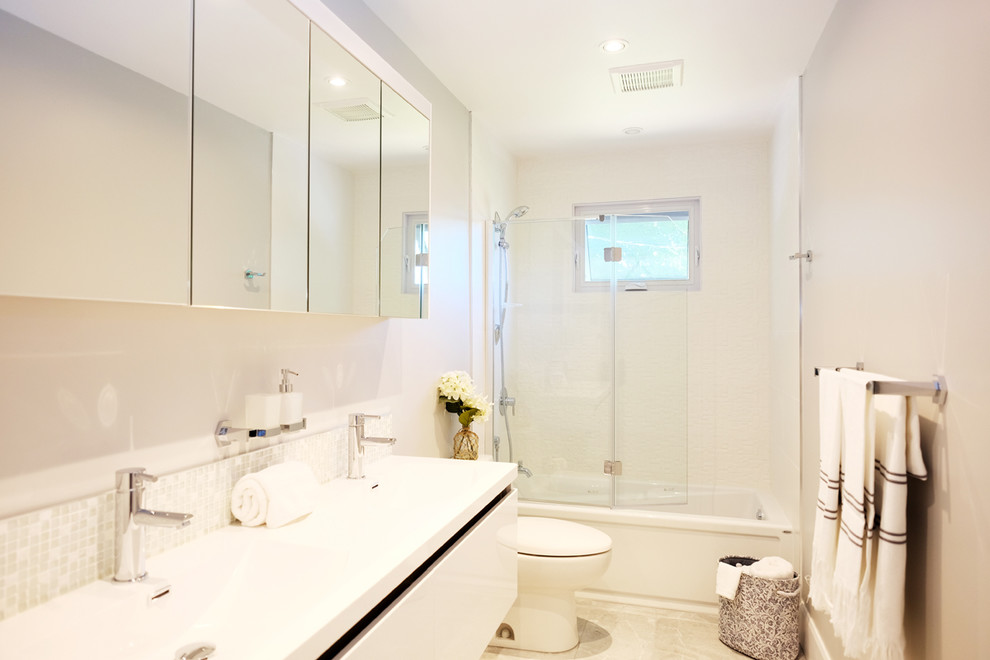 Design ideas for a small contemporary master bathroom in Montreal with flat-panel cabinets, white cabinets, an alcove tub, a shower/bathtub combo, a one-piece toilet, white tile, porcelain tile, grey walls, porcelain floors, an undermount sink and solid surface benchtops.