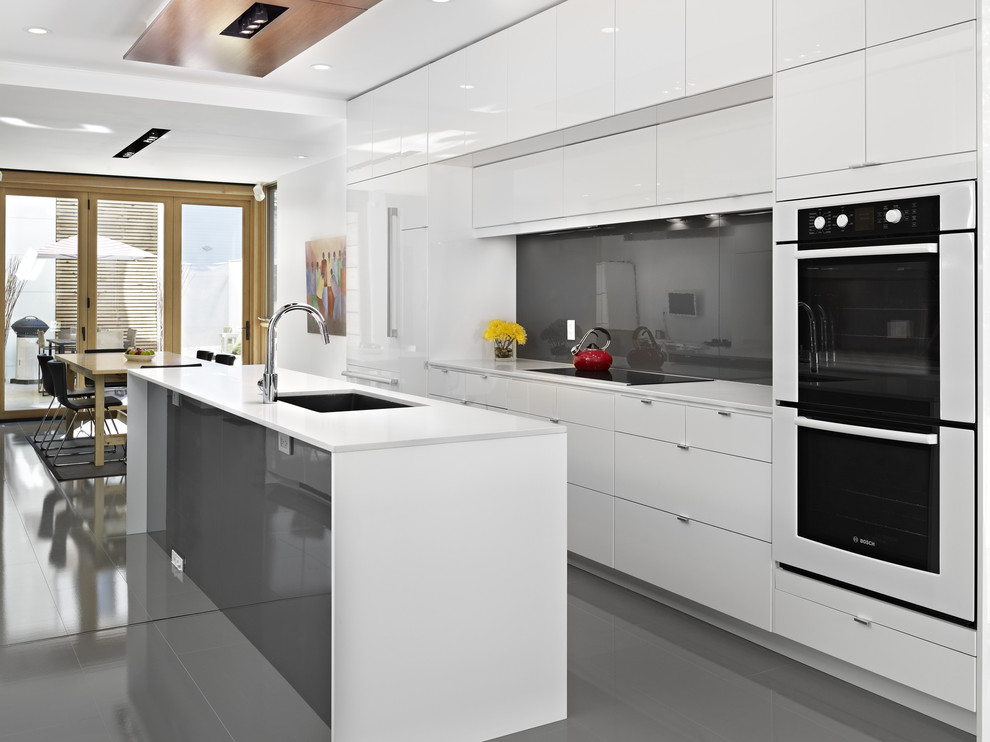 Inspiration for a contemporary galley eat-in kitchen in Edmonton with an undermount sink, flat-panel cabinets, white cabinets, black splashback, glass sheet splashback, white appliances, grey floor and white benchtop.
