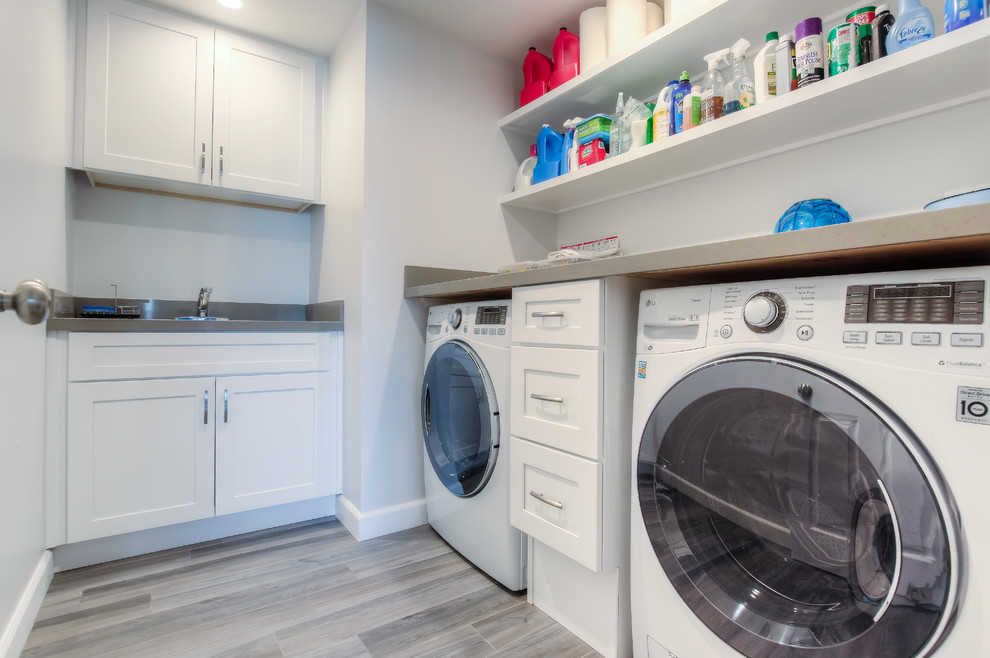 Design ideas for a mid-sized transitional l-shaped dedicated laundry room in Los Angeles with shaker cabinets, white cabinets, white walls, a side-by-side washer and dryer, an undermount sink, concrete benchtops, laminate floors and brown floor.