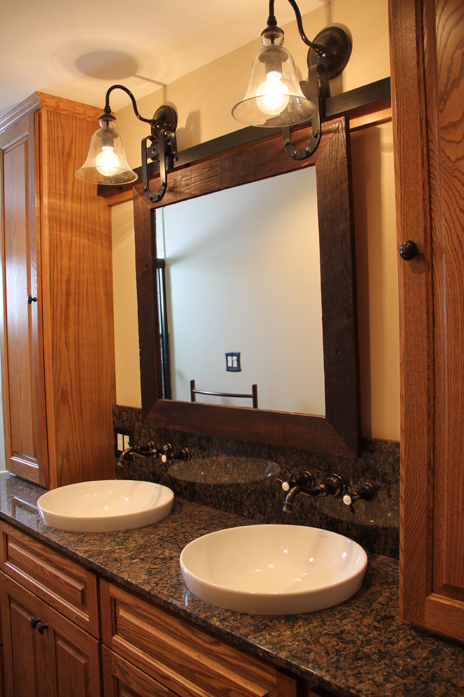 This is an example of a transitional bathroom in Columbus with a vessel sink, an undermount tub, a shower/bathtub combo, a two-piece toilet, raised-panel cabinets, medium wood cabinets, granite benchtops, brown tile, porcelain tile, beige walls and porcelain floors.
