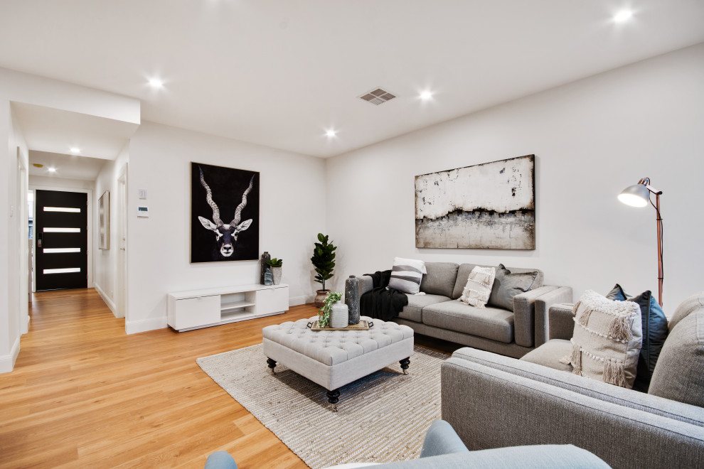 This is an example of a mid-sized contemporary open concept family room in Adelaide with white walls, laminate floors and brown floor.
