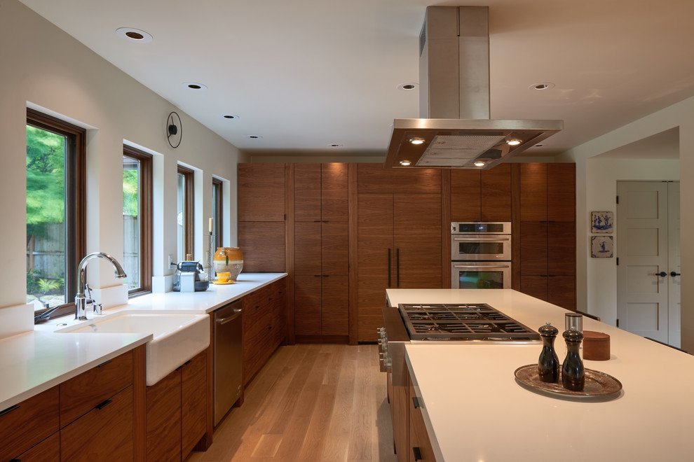 Inspiration for a mid-sized midcentury l-shaped eat-in kitchen in Seattle with a farmhouse sink, flat-panel cabinets, medium wood cabinets, quartz benchtops, white splashback, stainless steel appliances, light hardwood floors and with island.