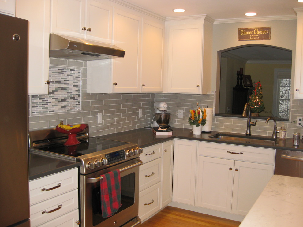 Example of a transitional l-shaped medium tone wood floor eat-in kitchen design in Boston with an undermount sink, white cabinets, quartz countertops, stainless steel appliances, an island, shaker cabinets, green backsplash, subway tile backsplash and black countertops