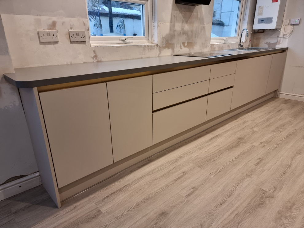 Design ideas for a large modern single-wall kitchen in London with quartz worktops, a single-bowl sink, flat-panel cabinets, grey cabinets, white splashback, porcelain splashback, integrated appliances, lino flooring and an island.