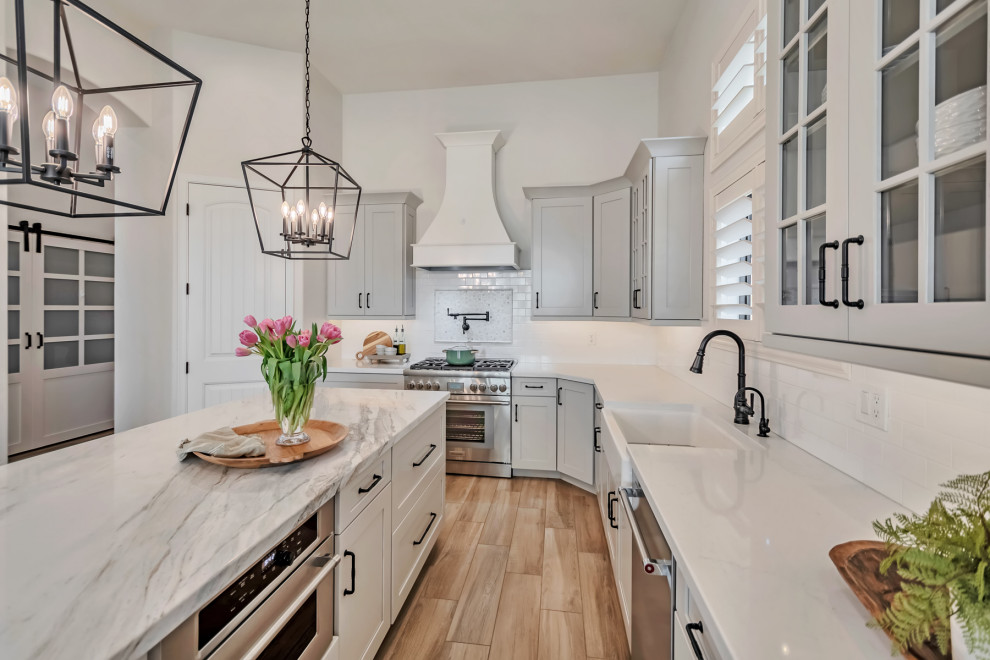 Kitchen - large transitional u-shaped porcelain tile, brown floor and exposed beam kitchen idea in Phoenix with a farmhouse sink, shaker cabinets, gray cabinets, quartzite countertops, white backsplash, porcelain backsplash, stainless steel appliances, an island and white countertops