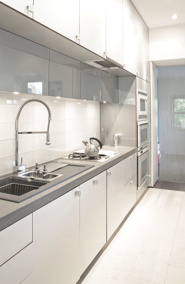Photo of a mid-sized contemporary galley eat-in kitchen in DC Metro with a drop-in sink, flat-panel cabinets, white cabinets, terrazzo benchtops, white splashback, glass tile splashback, stainless steel appliances, limestone floors and with island.