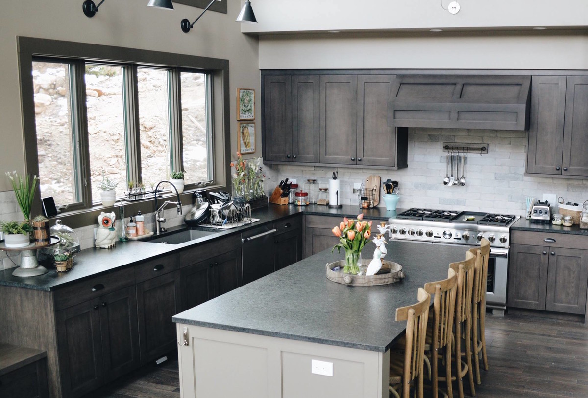 Large country l-shaped open plan kitchen in Denver with an undermount sink, shaker cabinets, grey cabinets, grey splashback, stone tile splashback, stainless steel appliances, dark hardwood floors, with island and grey floor.